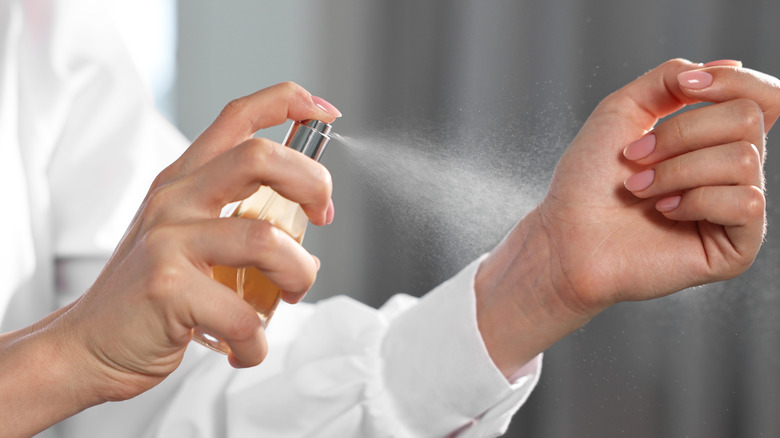 Vrouw spuit parfum op haar pols terwijl ze binnenshuis is