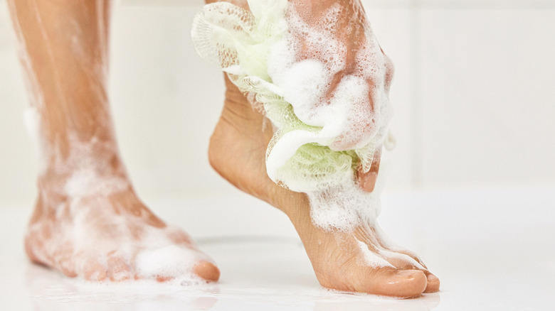 Persoon wast zijn voeten onder de douche met zeep en een spons