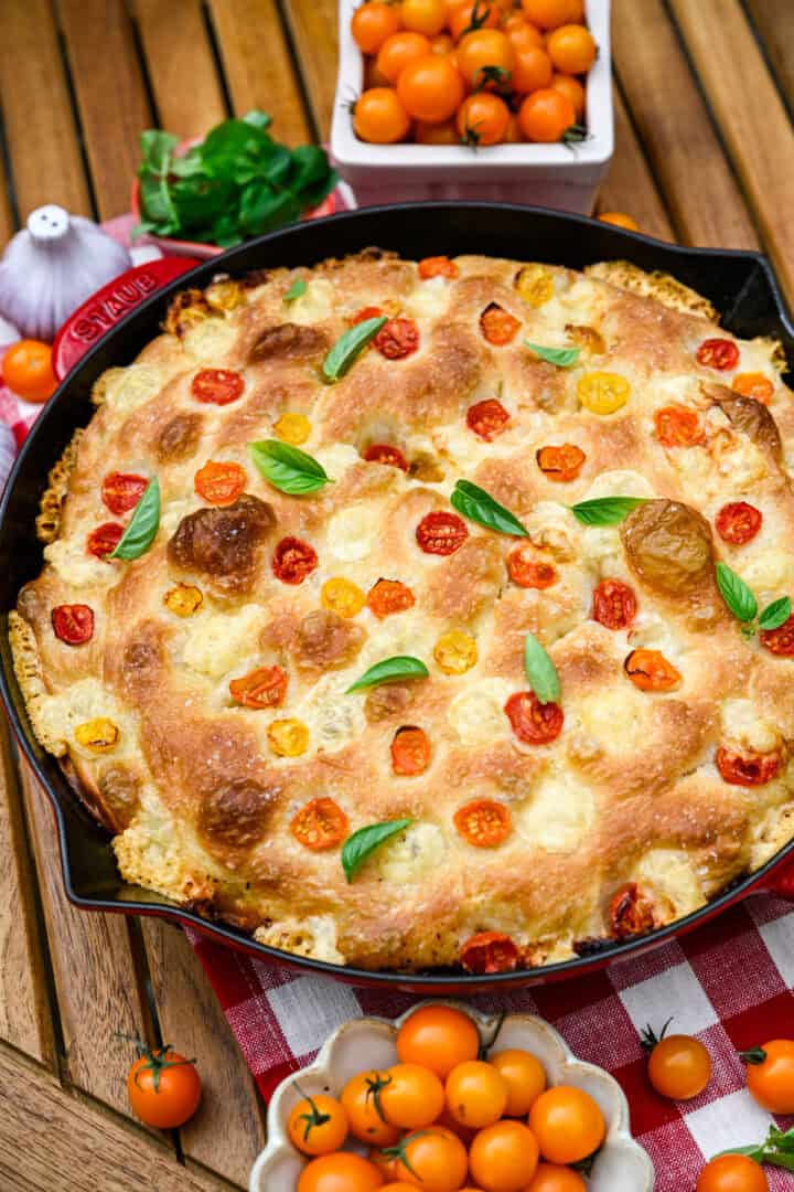 Bovenaanzicht van focaccia van tomatenbasilicum in een rode gietijzeren koekepan.