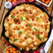 Bovenaanzicht van focaccia van tomatenbasilicum in een rode gietijzeren koekepan.