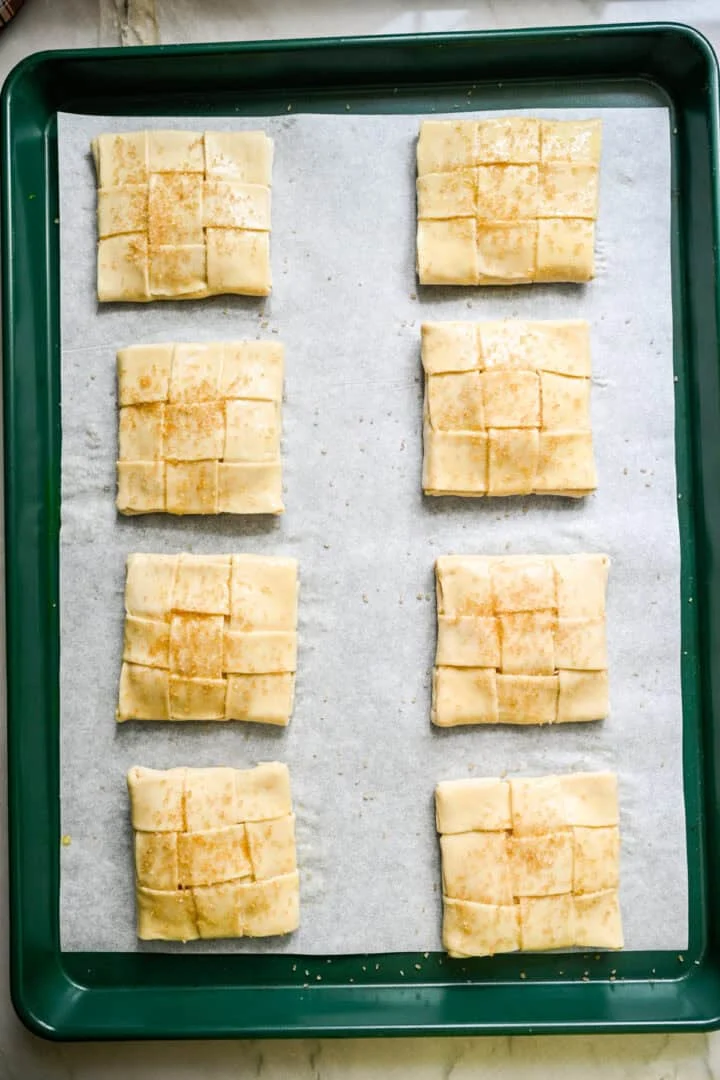 Bovenaanzicht van 8 ongebakken appeltaarten op een met perkament beklede bakplaat.