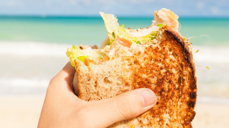De hand van iemand die een gedeeltelijk opgegeten broodje vasthoudt op het strand