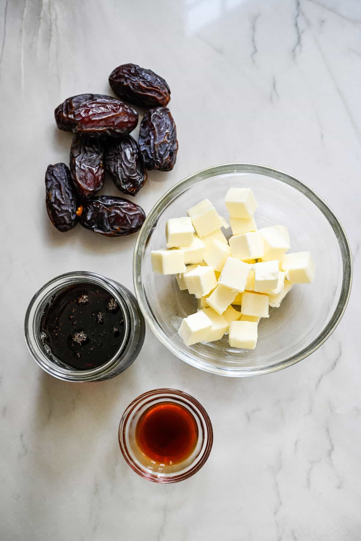 bovenaanzicht van boter, dadels, ahornsiroop en vanille-extract om ingrediënten voor dadelkaramelsaus te tonen.