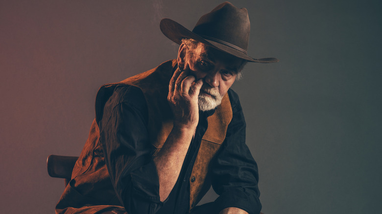 oudere cowboy die er versleten uitziet terwijl hij op een kleine stoel zit