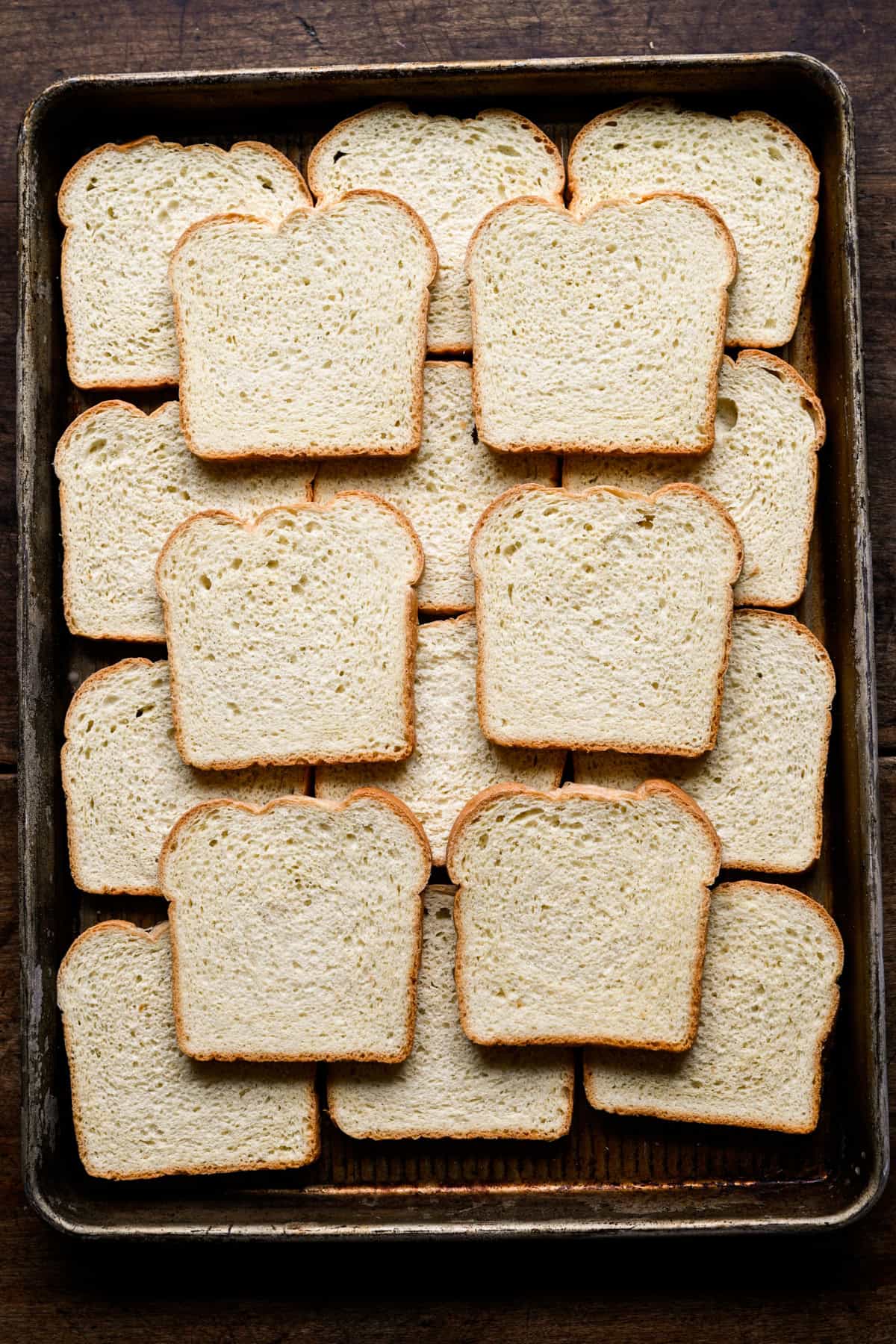 Bovenaanzicht van plakjes bevroren wit sandwichbrood, uitgespreid over een metalen plaat.
