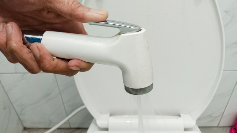 Een man die een bidetsproeier boven een toilet houdt