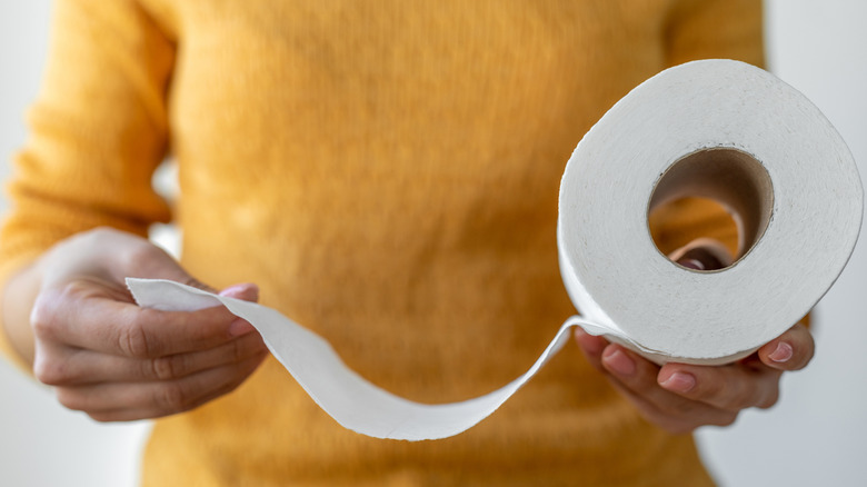 Een vrouw houdt een rol wc-papier vast en haalt er verschillende vellen uit