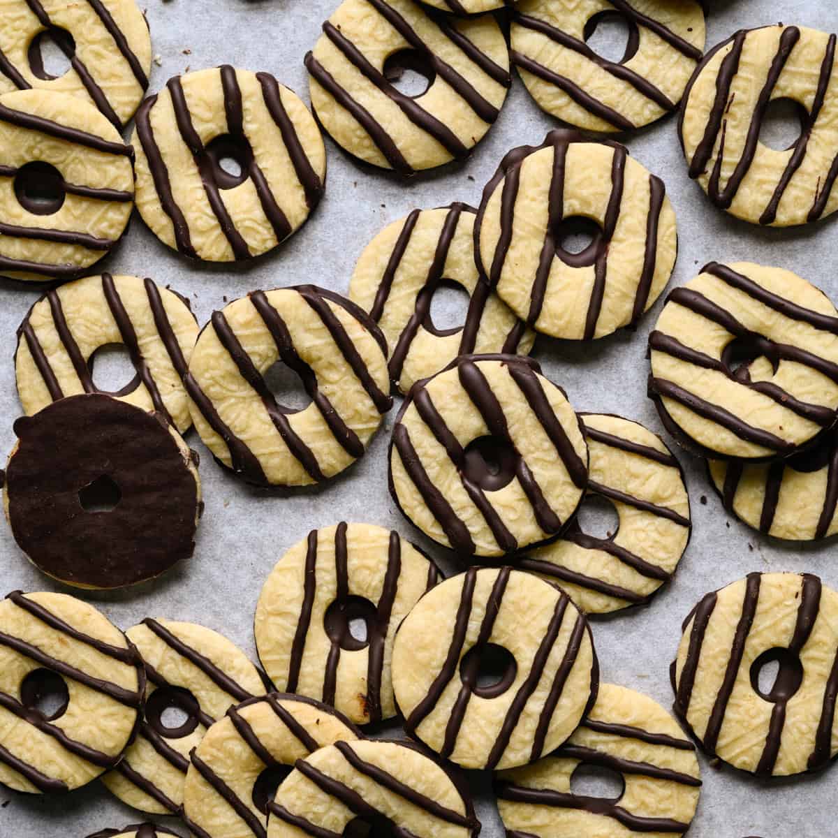 Overlappende zelfgemaakte fudge-streepkoekjes verspreid over perkamentpapier, waarbij één koekje omgedraaid is om de met chocolade bedekte onderkant te laten zien.