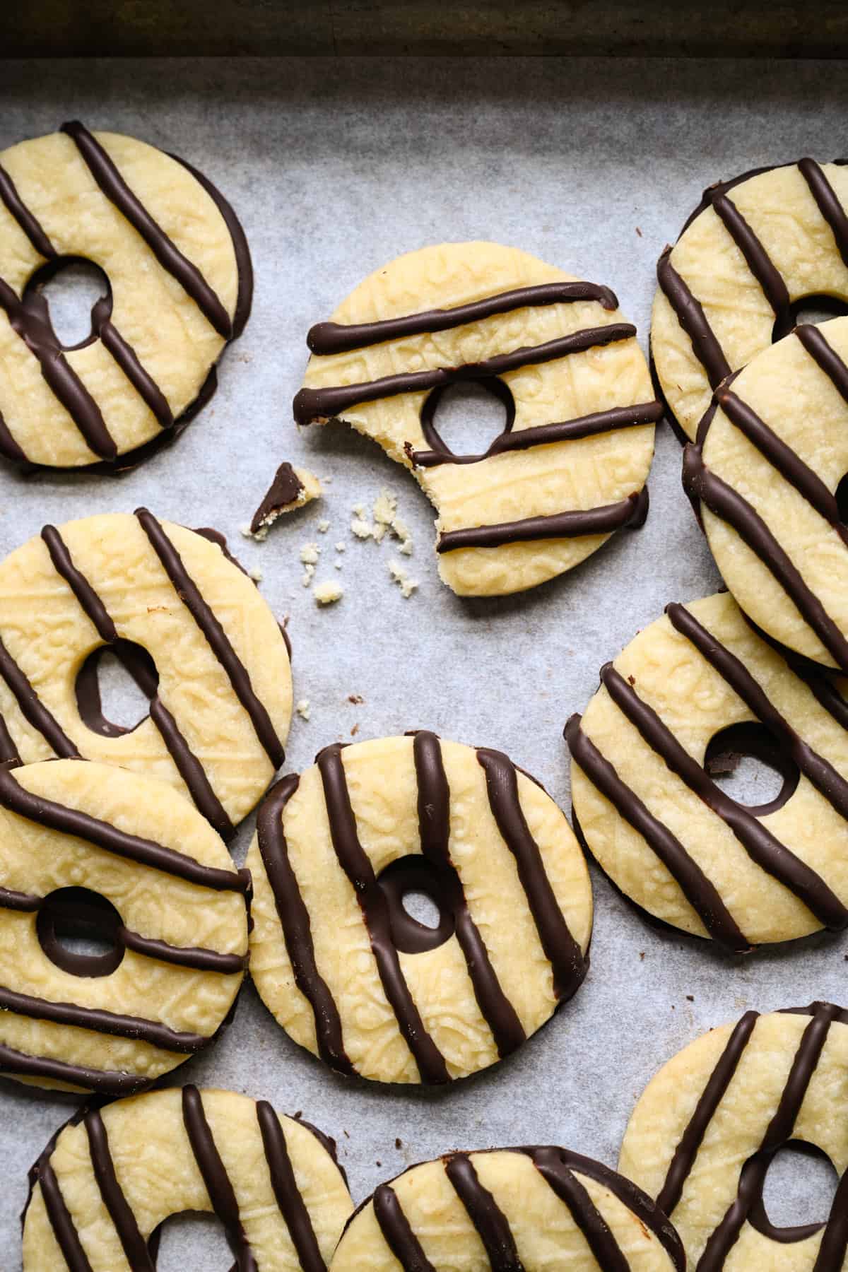 Zelfgemaakt fudge-streepkoekje met een stukje eruit en een paar kruimels ernaast, omringd door nog meer chocoladegestreepte zandkoekkoekjes op perkamentpapier.