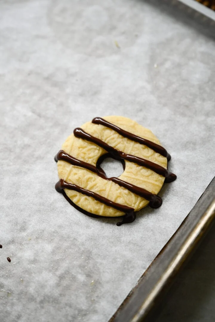 Enkel ringvormig zandkoekkoekje met een met chocolade bedekte onderkant en vier strepen van pure chocolade besprenkeld over de bovenkant.