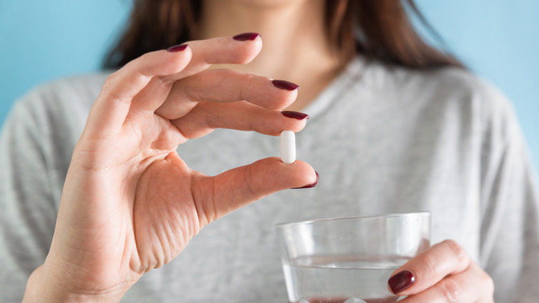 vrouw die een statine in haar hand houdt die ze met een glas water gaat innemen