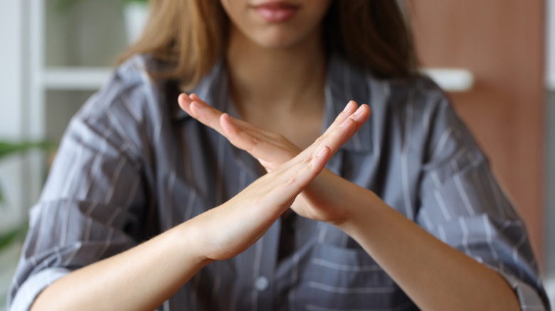 vrouw kruist haar armen in de vorm van een X terwijl ze aan een tafel zit
