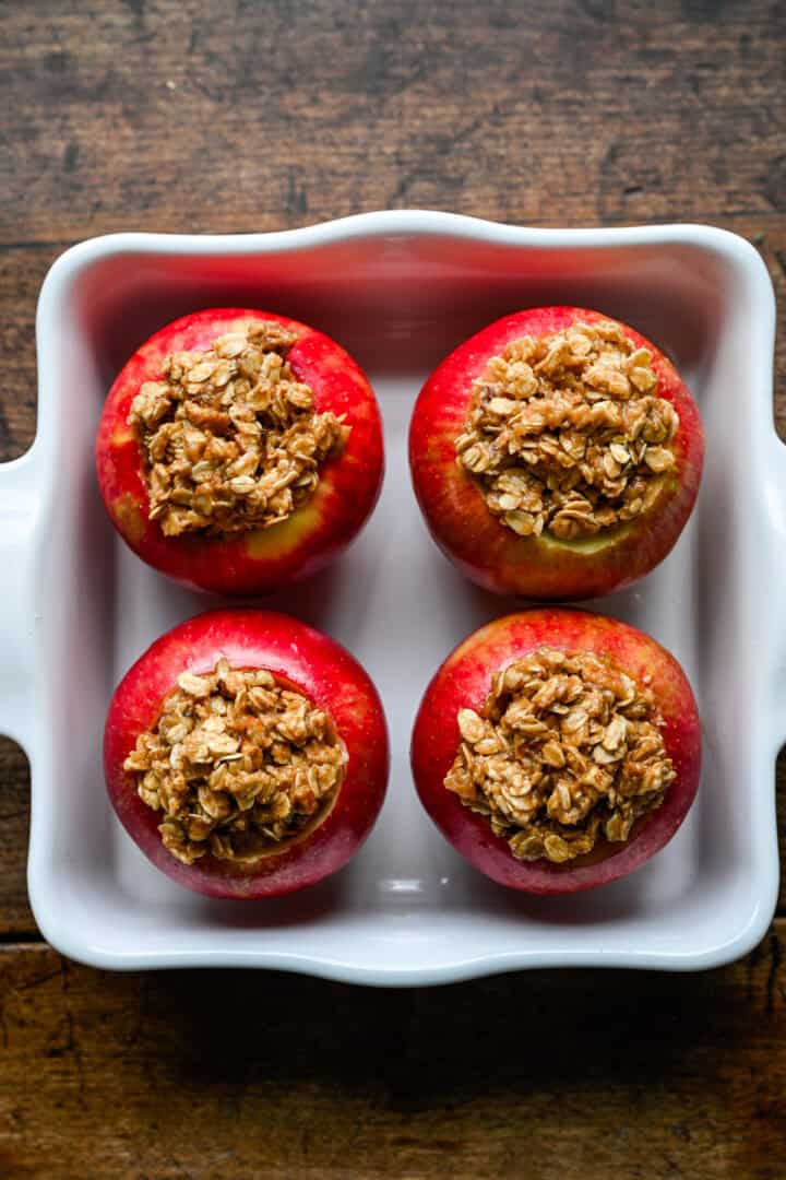 Appels zonder klokhuis verpakt met haverkruimelvulling in een witte ovenschaal vóór het bakken.