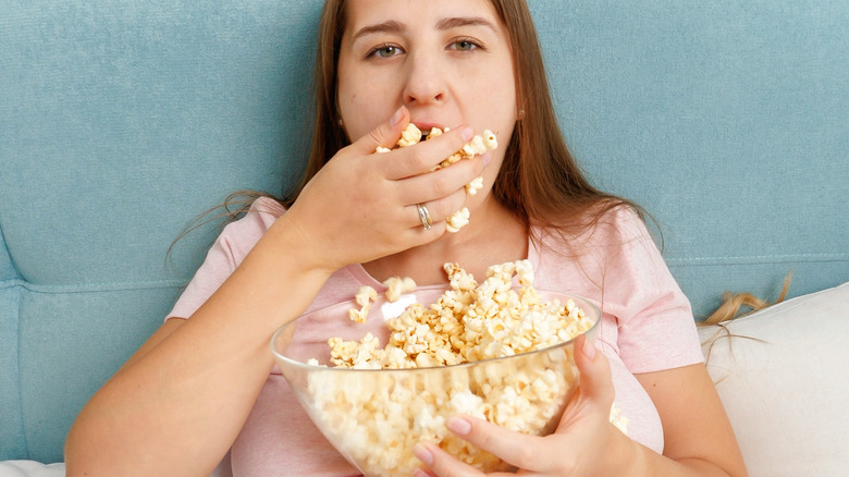 vrouw die naar de camera kijkt en een handvol popcorn eet terwijl ze in rustpositie is