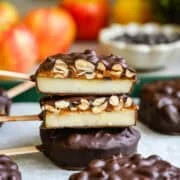 Vooraanzicht van twee gehalveerde met chocolade bedekte appelschijfjes, gestapeld om lagen appel, dadelpasta en pinda's te tonen, met appels erachter.