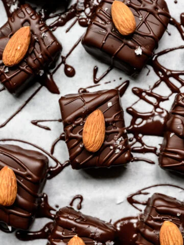 Close-up van met chocolade omhulde repen gegarneerd met hele amandelen en schilferig zout op perkament.
