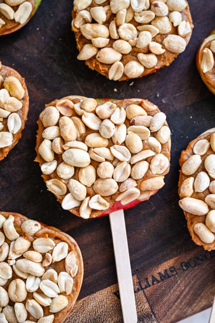 Close-up van appelschijfjes op ijsstokjes, gegarneerd met dadelspread en een laag geroosterde pinda's.