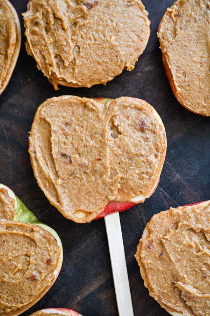 Close-up van appelschijfjes op ijslollystokjes, verspreid met een laagje pindakaas-dadelspread.