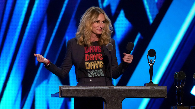 Julia Roberts heft haar armen op terwijl ze op het podium van een evenement spreekt