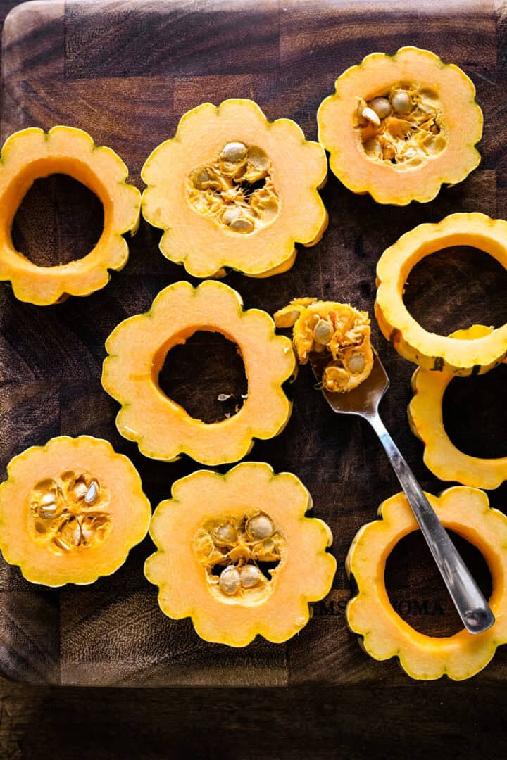 Bovenaanzicht van delicata squashrondes op een houten plank, de zaden eruit geschept met een lepel.