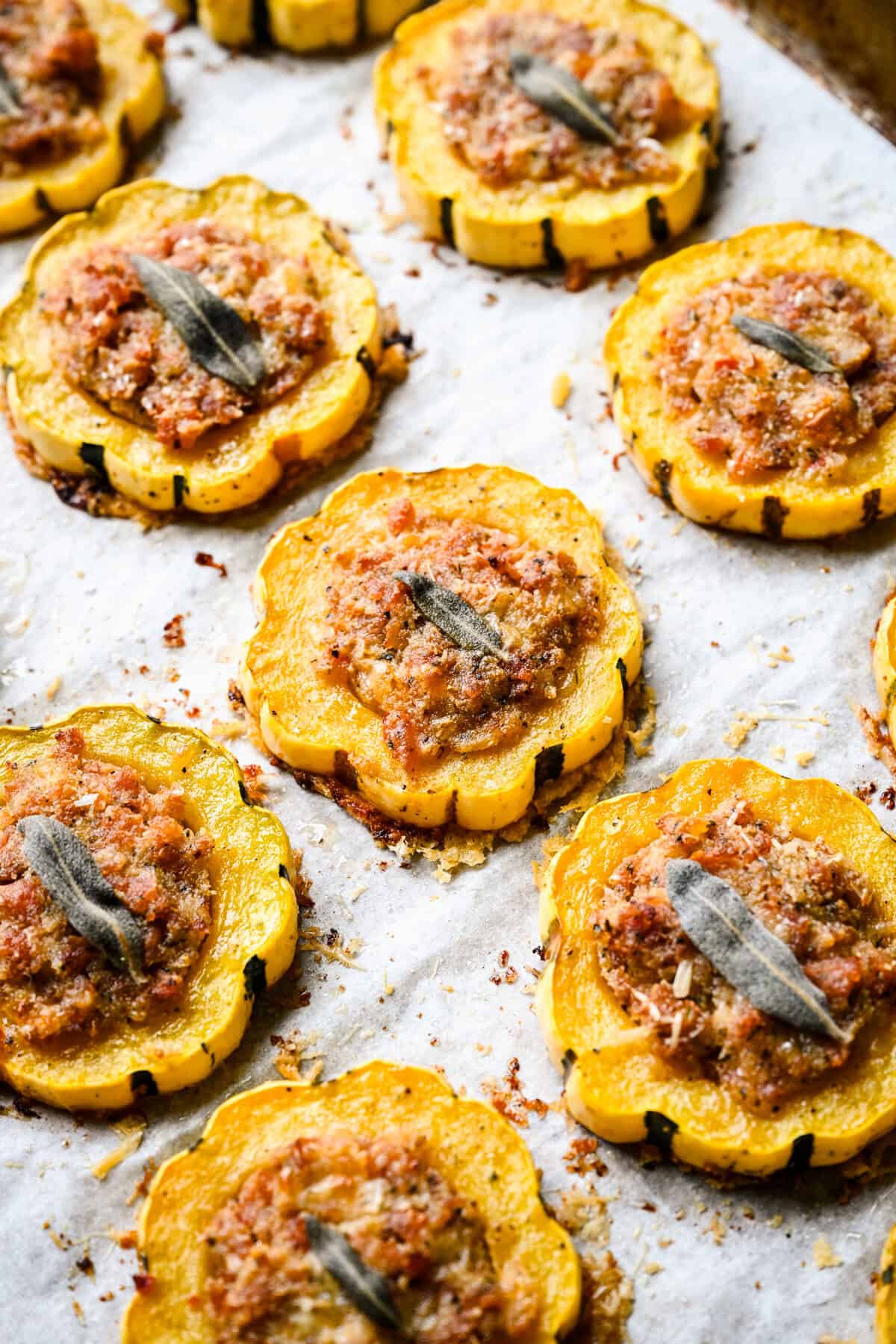 45 graden zicht op gebakken worst gevulde delicata squashringen op een met perkament beklede pan.