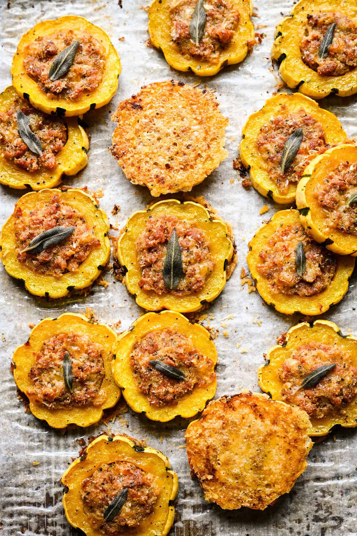 Bovenaanzicht van gevulde delicata-pompoenringen en twee Parmezaanse kaaschips op een met perkament beklede pan.