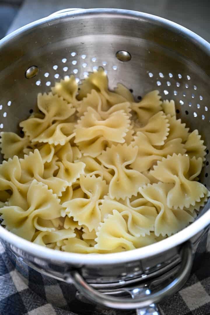 Bovenaanzicht van gekookte vlinderdaspasta die uitlekt in een metalen vergiet in een pot.