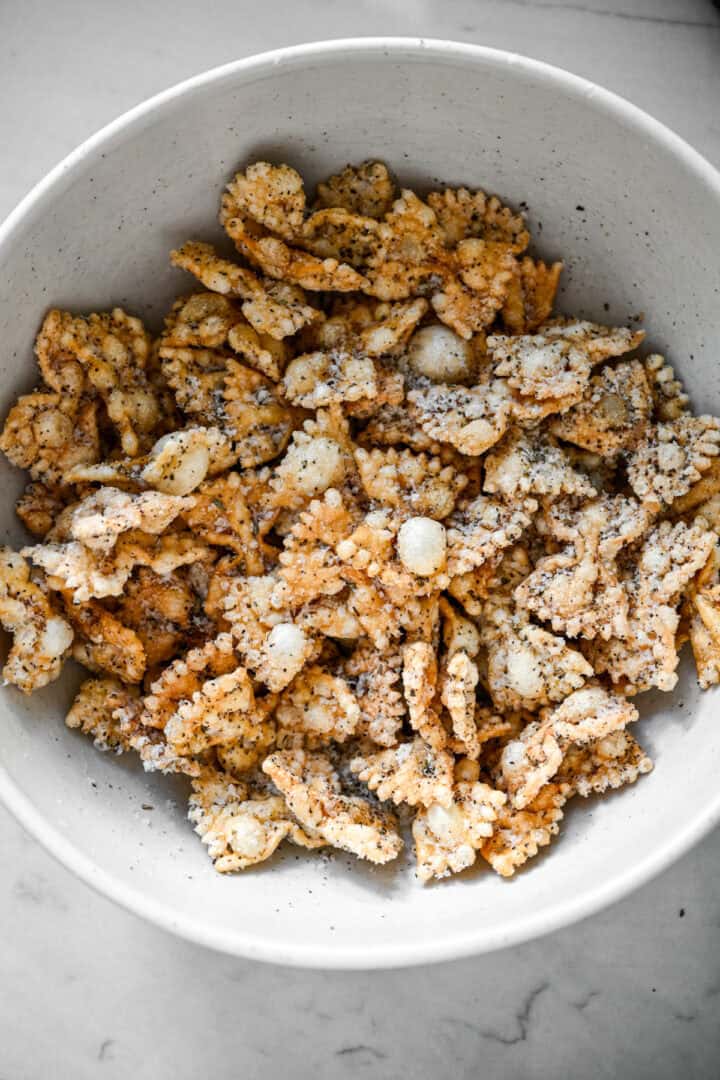Bovenaanzicht van gepofte pasta gegooid met geraspte Parmezaanse kaas en zwarte peper in een witte kom.