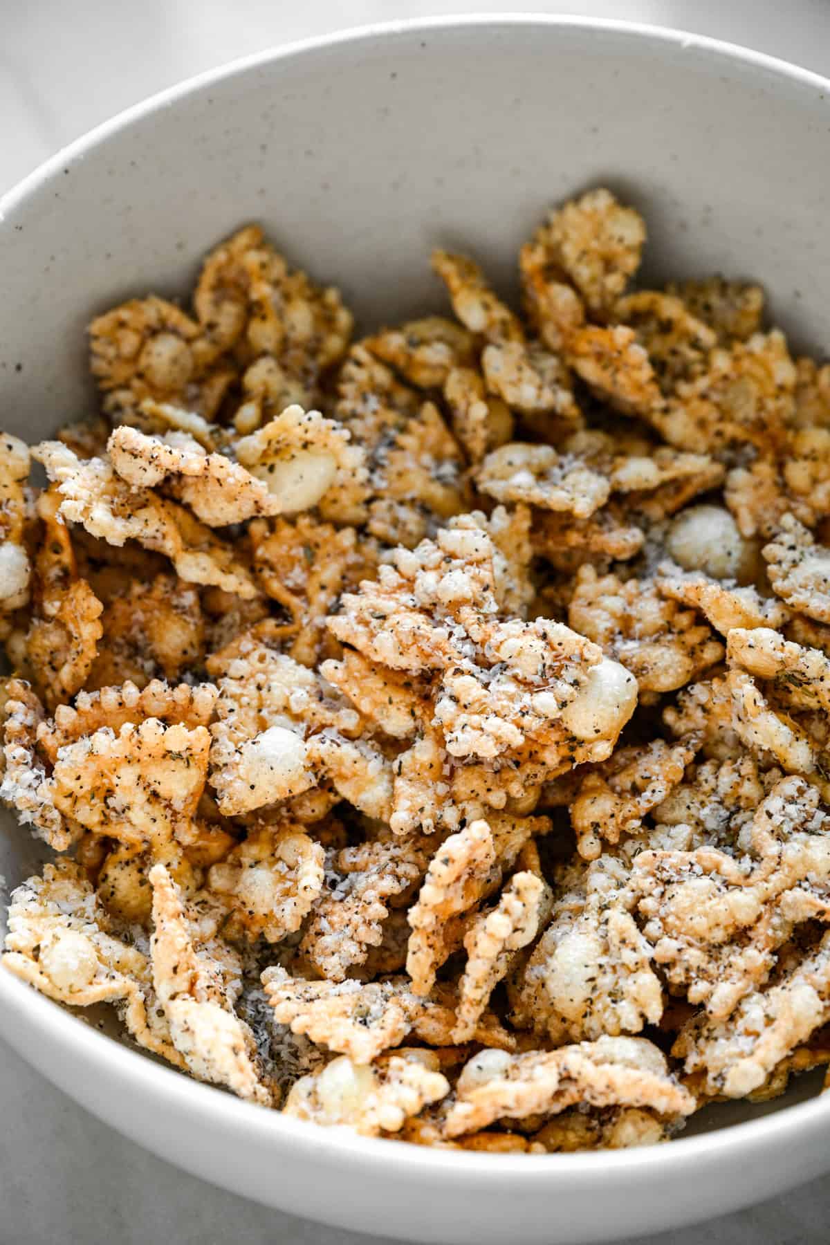45 graden zicht op gekruide gepofte pasta die een wit gespikkelde kom vult.
