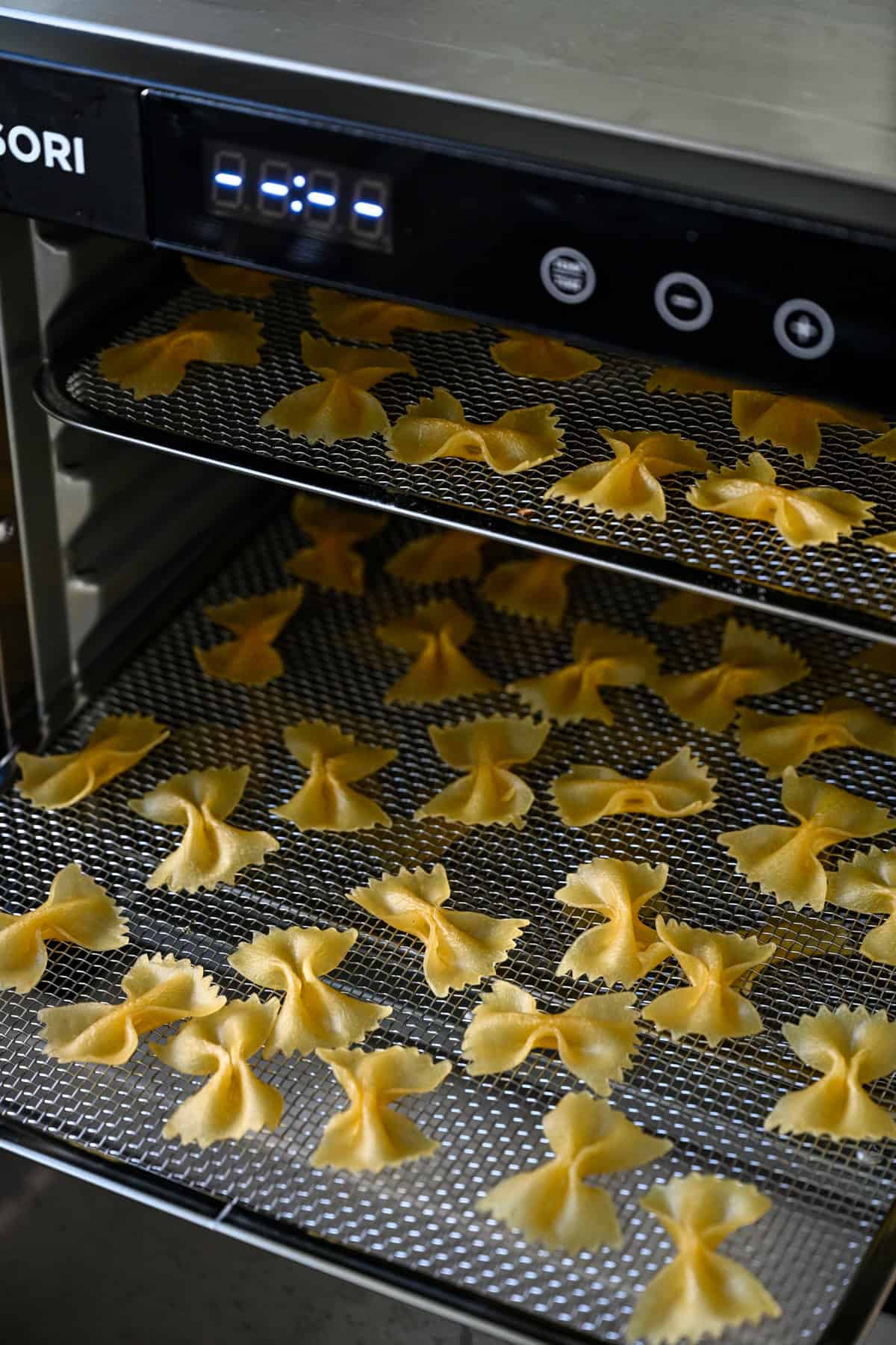 Vooraanzicht van twee dehydratorladen met vlinderdaspasta die in de machine drogen.