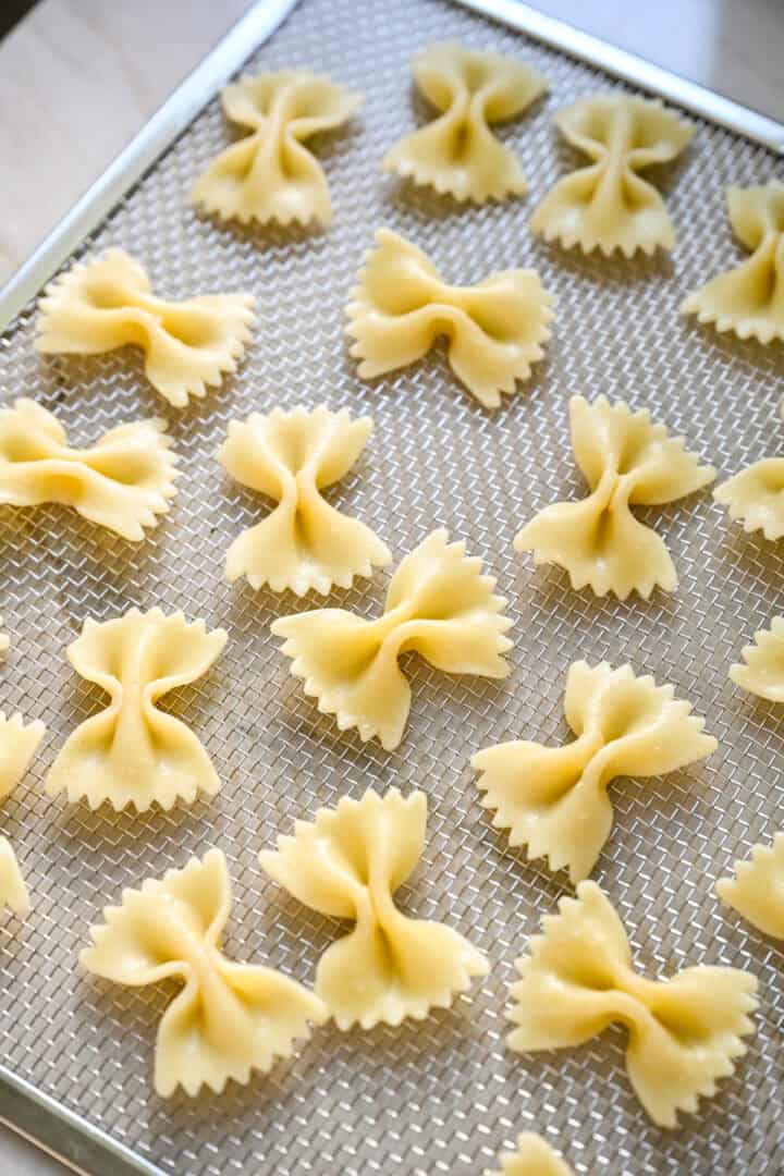 45 graden zicht op gekookte vlinderdaspasta, uitgespreid op een rooster van dehydratatiebak.
