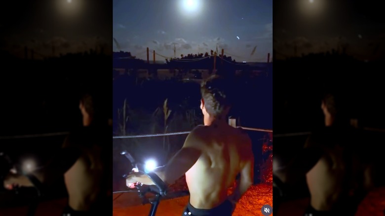 Ryan Seacrest staart van achteren naar de lucht terwijl hij shirtloos is met een fiets