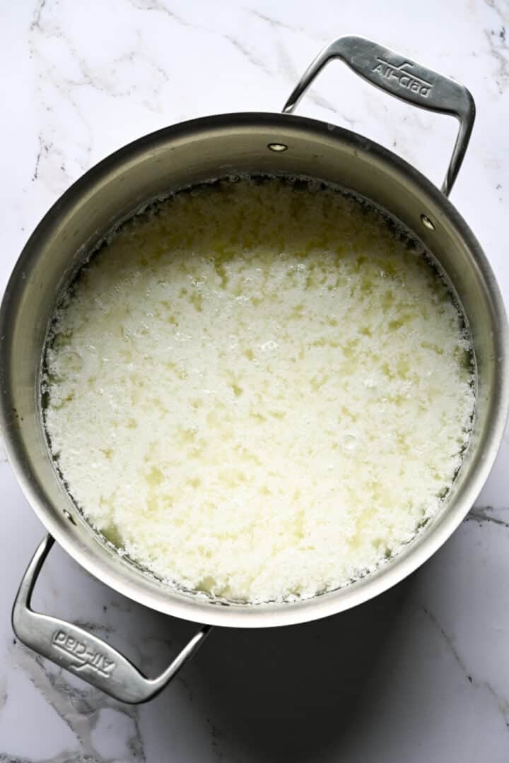 Bovenaanzicht van kwarkwrongel gescheiden van wei in een All-Clad pot op marmer