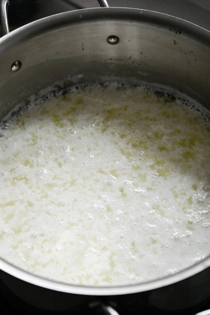 45 graden weergave van melk die zich in een roestvrijstalen pot scheidt in wrongel en wei na toevoeging van azijn