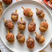 Bovenaanzicht van eikelkaasballetjes met krakelingstengels op een witte plaat, met crackers op een pompoenbord en decoratieve eikels ernaast.