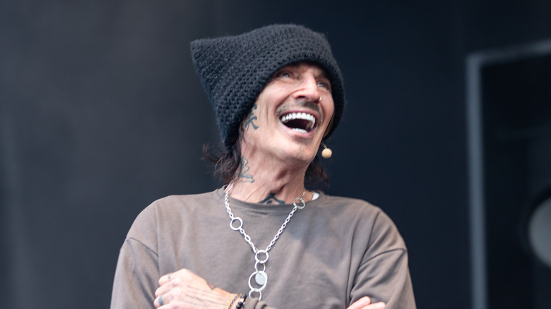 Tommy Lee staat lachend op het podium met een gebreide muts en een T-shirt met lange mouwen op